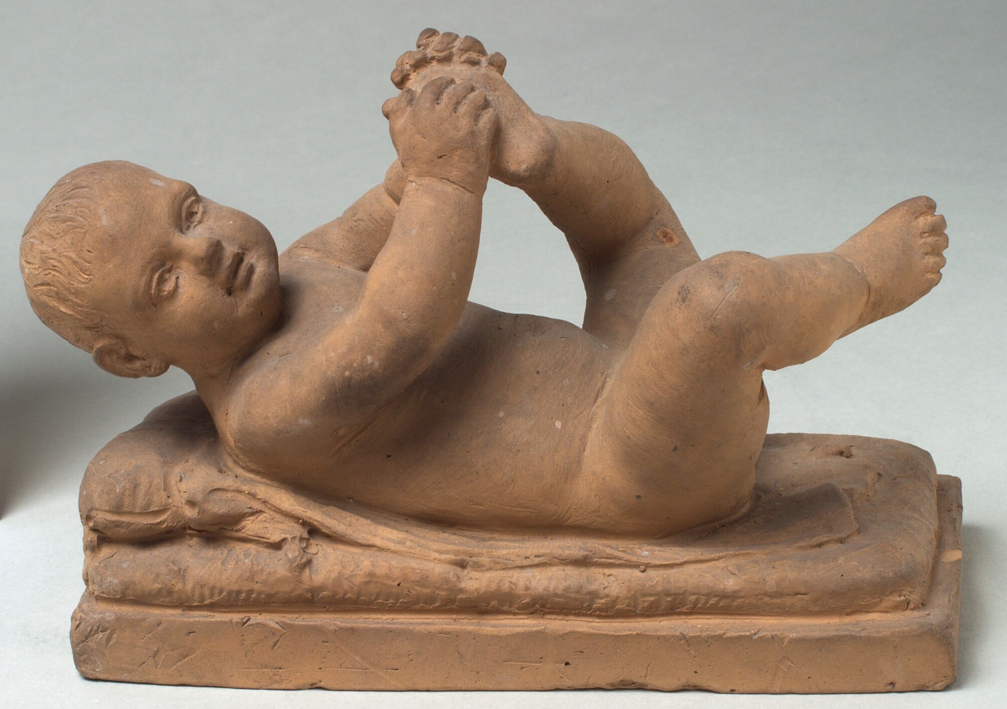 Liggende nøgent barn, der leger med sin fod