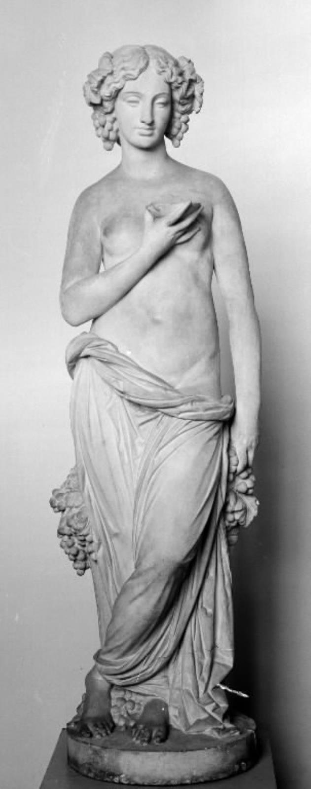 Høsten. Stående, halvt draperet kvinde med en skål i hånden og druer og vinløv i håret