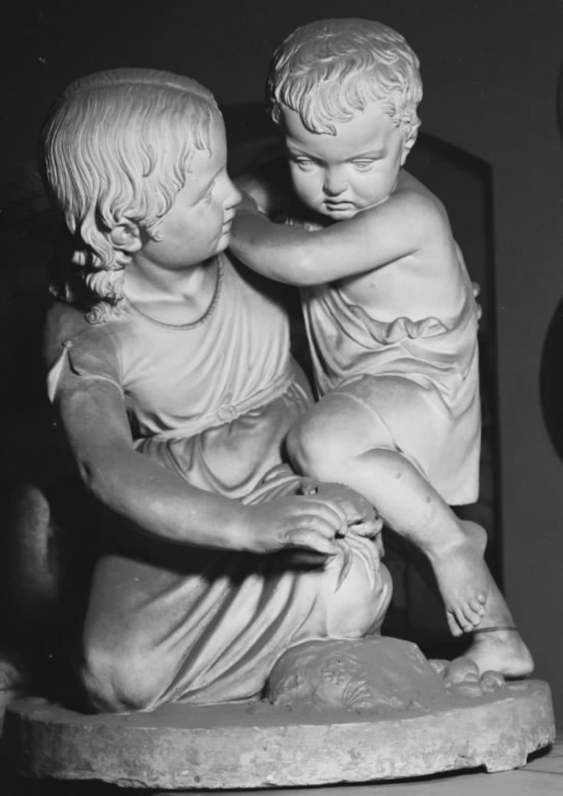 To børn med en krabbe. En lille pige, der ligger på knæ i sandet, viser en krabbe til en lille dreng